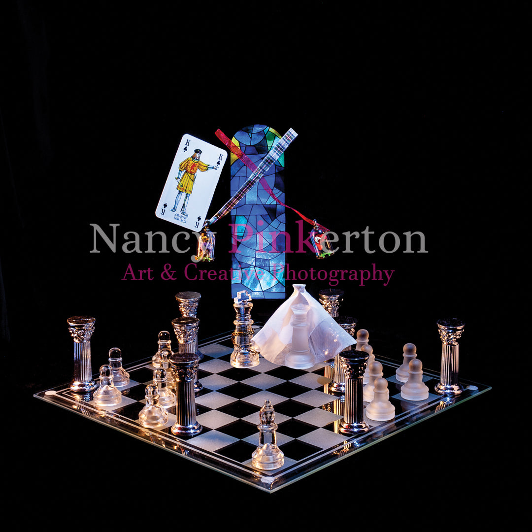 Photographic art print with image of a playing card featuring King James IV floating next to a thistle and a rose  just above a king and queen with a white veil above a glass chessboard laid out with silver pillars and chess pieces.