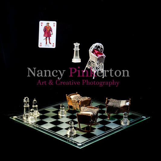 Photographic art print with image of a playing card featuring King James V and a fancy white cradle floating above a glass chessboard laid our with chess pieces and 3 plain wooden cradles.