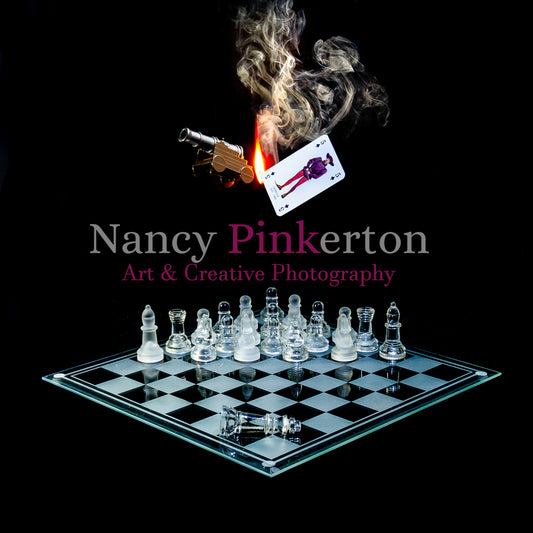 Photographic art print with image of a playing card featuring King James II next to a backfiring cannon represented using a flame and smoke, floating above a glass chessboard with chess pieces strategically place.