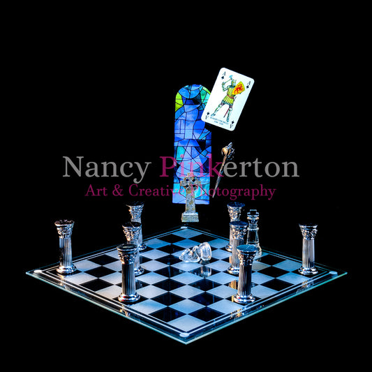 Photographic art print with image of a playing card featuring Robert Bruce, a sword, Celtic cross in front of a blue stained glass window floating above a glass chessboard with knight piece laying on its side surrounded by silver pillars.